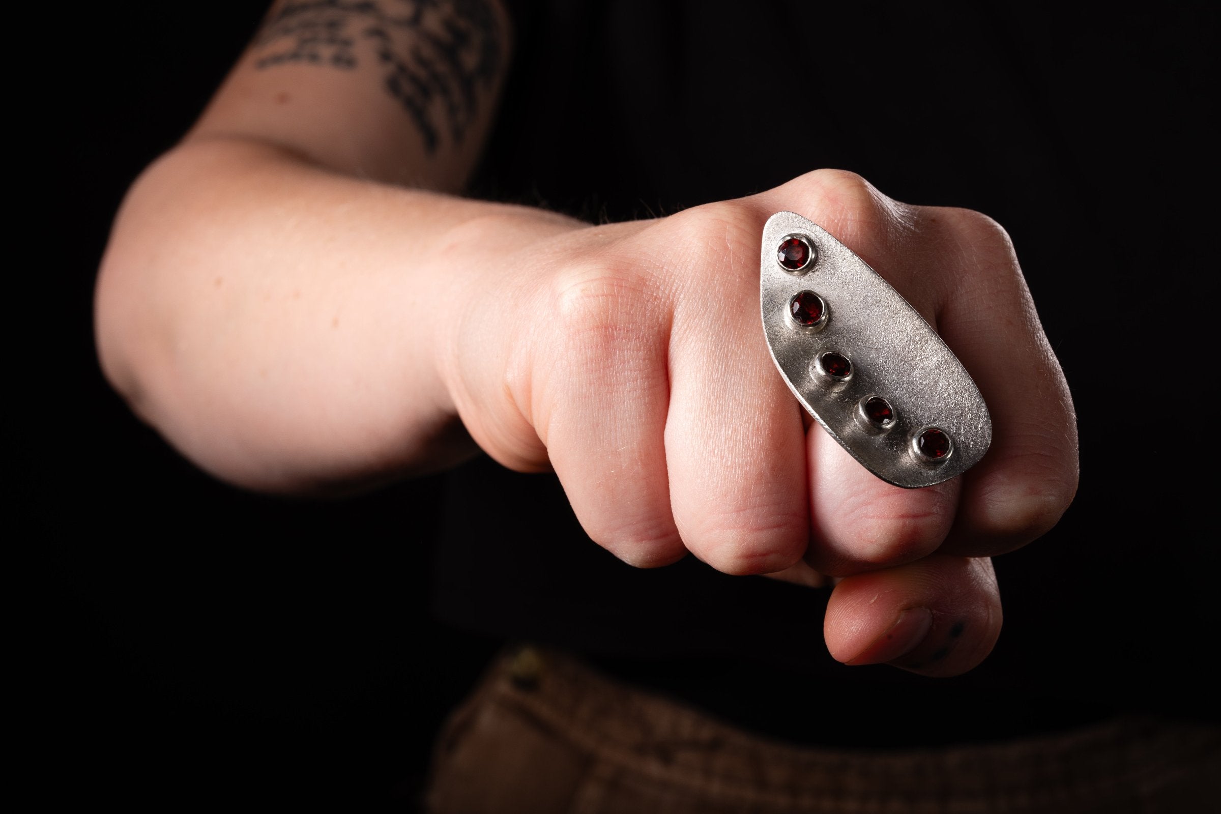 Big bold silver ring with frosted texture and five red garnets on a woman's hand punching forwards.