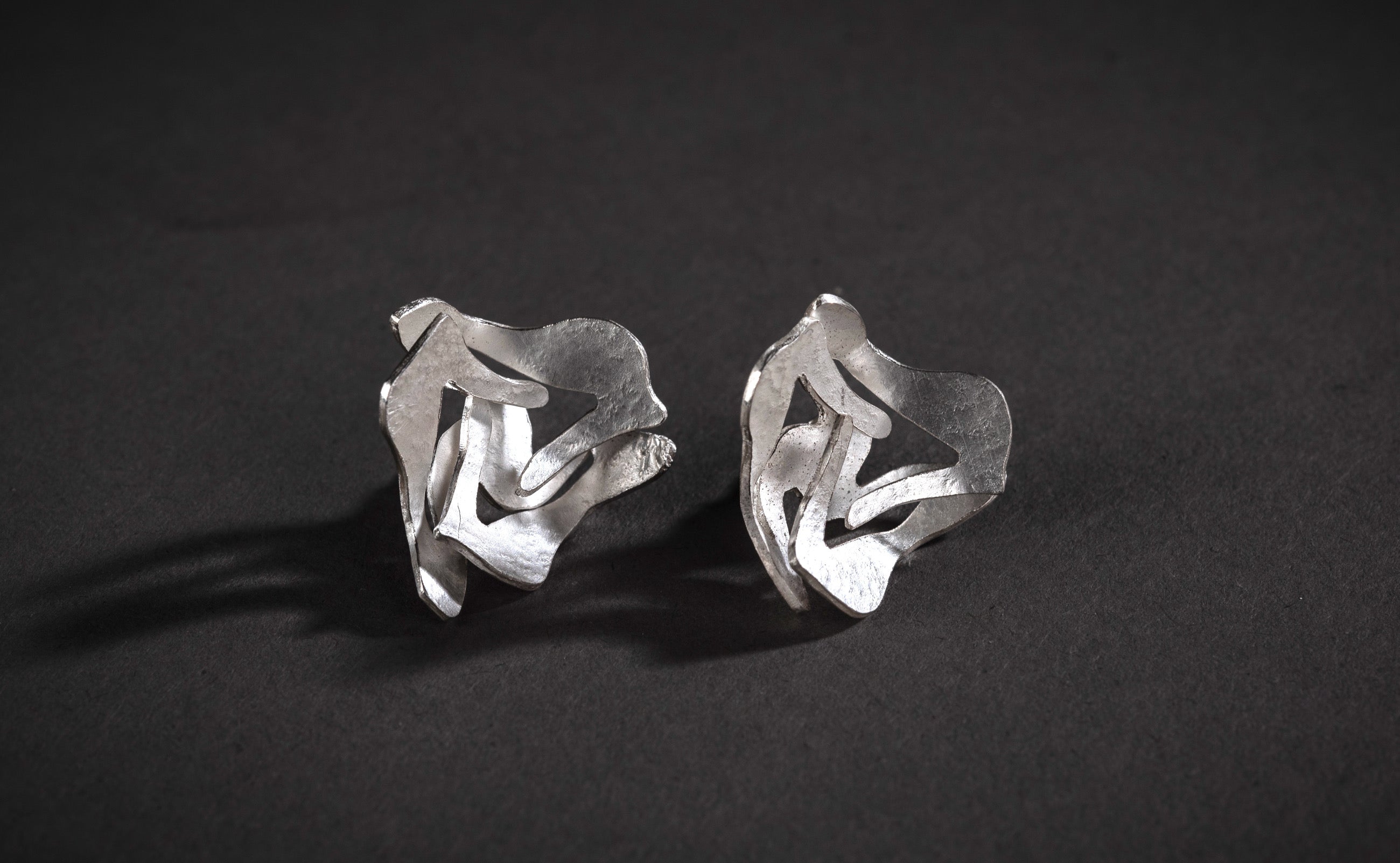 A pair of large textured silver ear studs made of pierced silver sheet in a contemporary floral-like design.