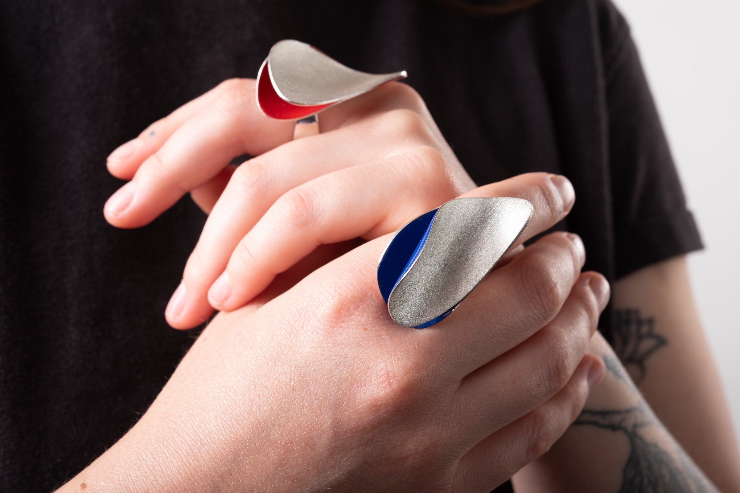 Two statement silver rings worn on the hands of a woman.  Each ring has a coloured enamel interior in red and in blue.