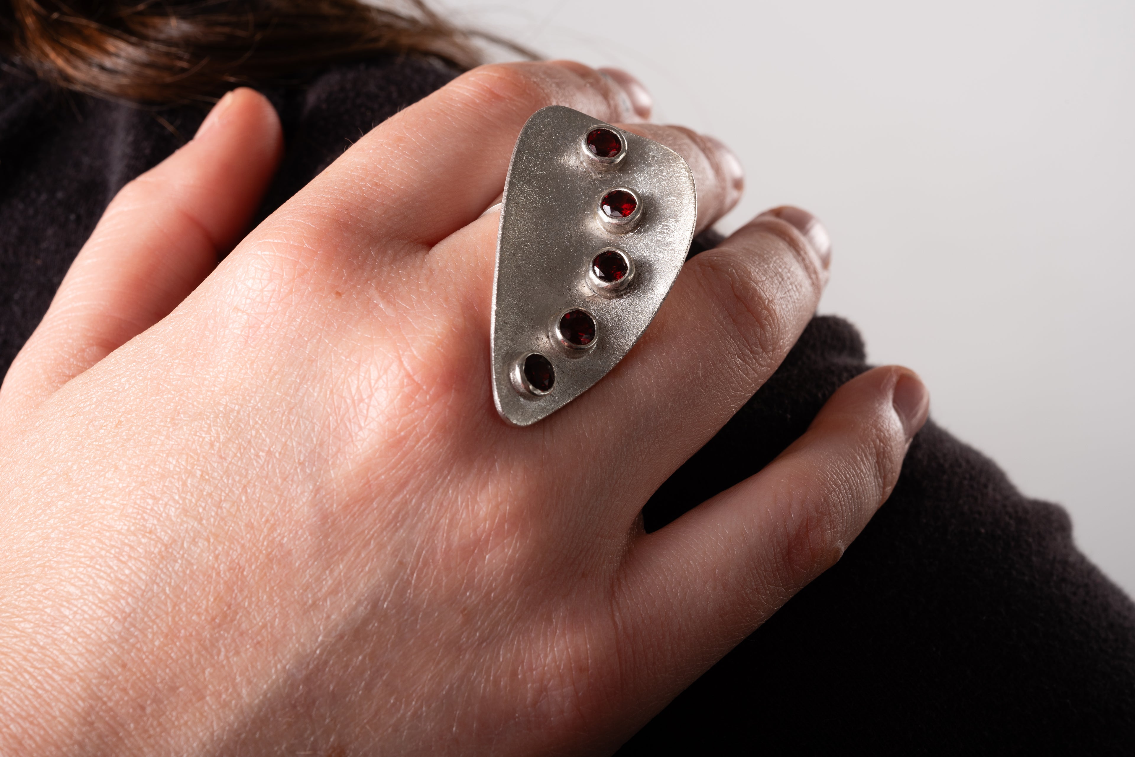 Large silver ring with a frosted finish and set with five bezel set garnets.  The ring shape is a curved asymmetric triangle with the faceted garnets set following the curve on one side.