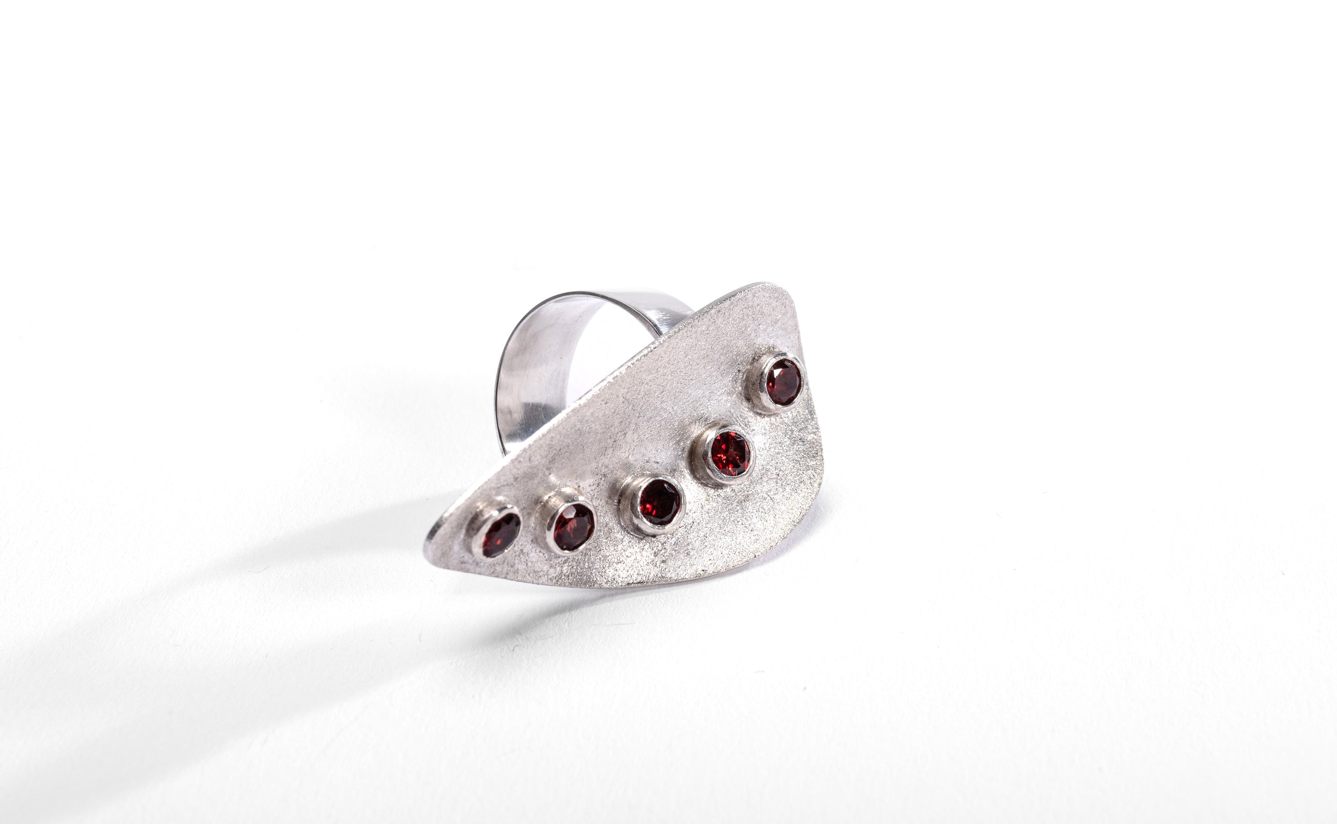 Large statement silver ring with frosted finish.  It has five large red garnets bezel set in a curve down the centre of the ring.