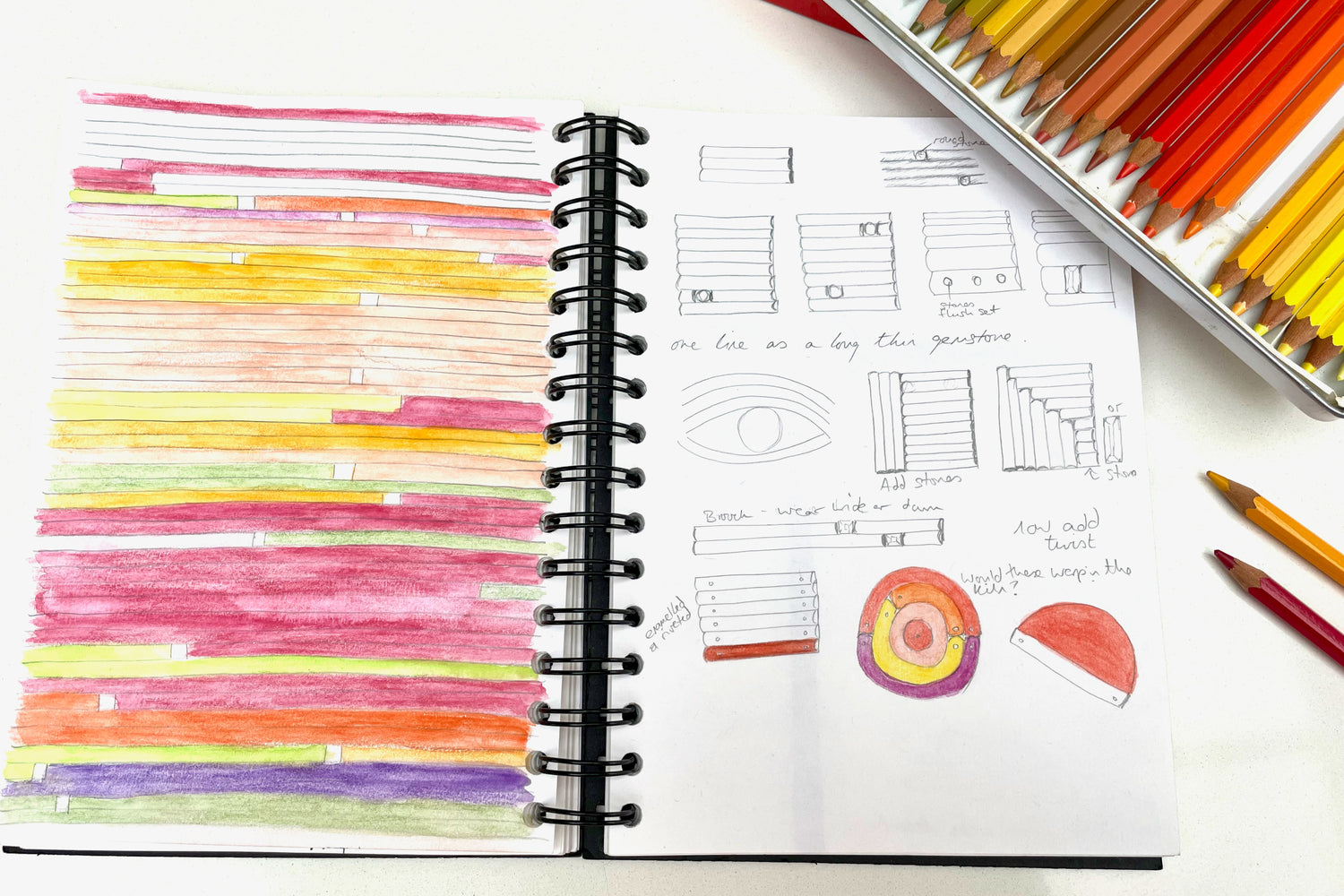 Open sketchbook and coloured pencils. shows colourful drawing and sketched contemporary jewellery designs.