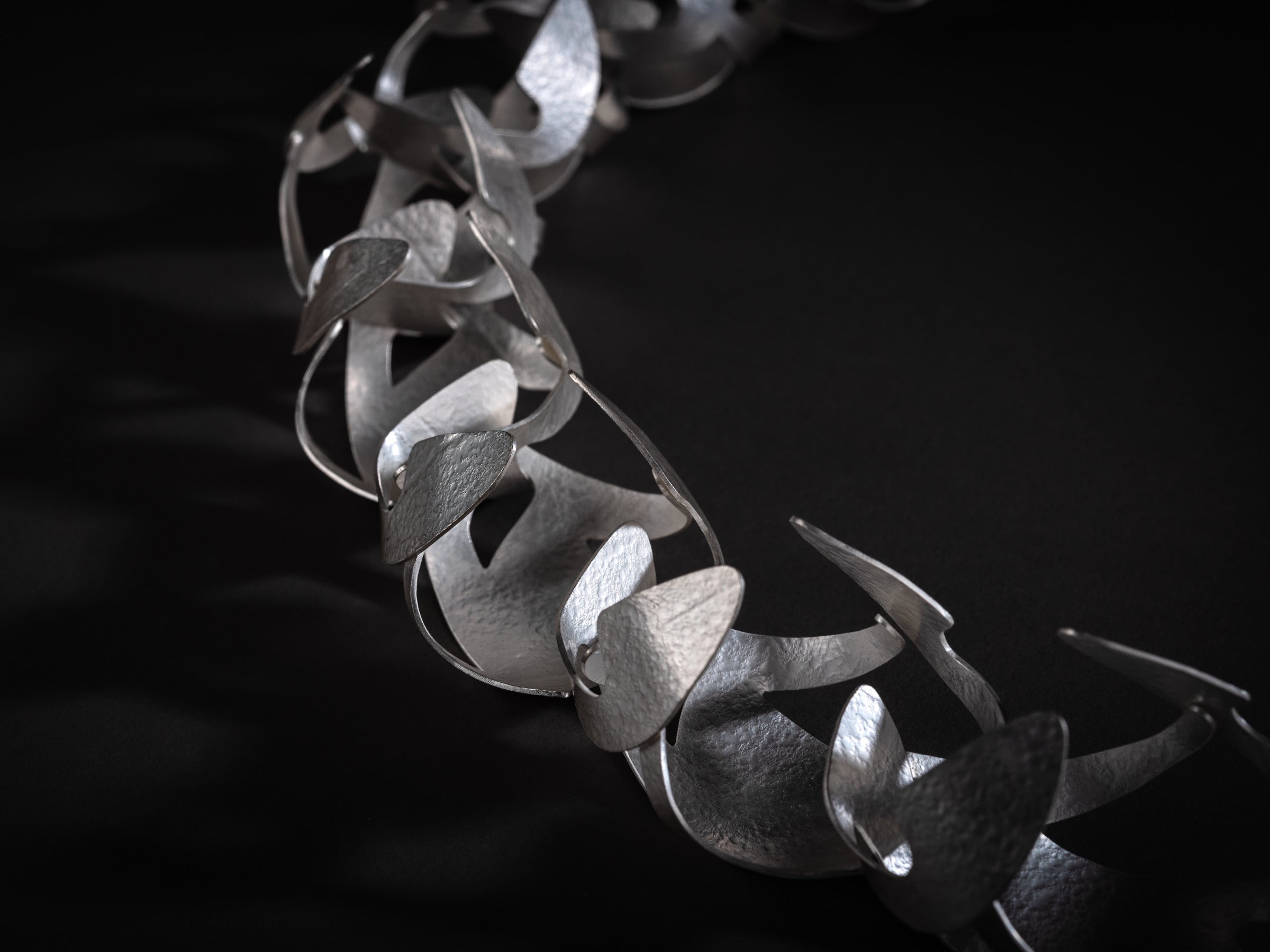 Close up of silver statement collar necklace with paper-like texture.  The necklace is made of repeating organic forms.