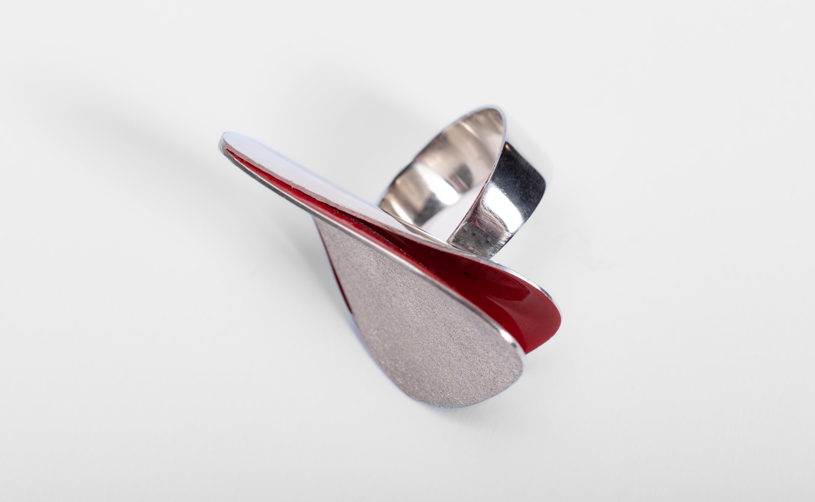 Unusual shaped silver ring with textured surface like frosting.  It has a curved band and two curved shapes about it with red enamel just visible  inside the curves.